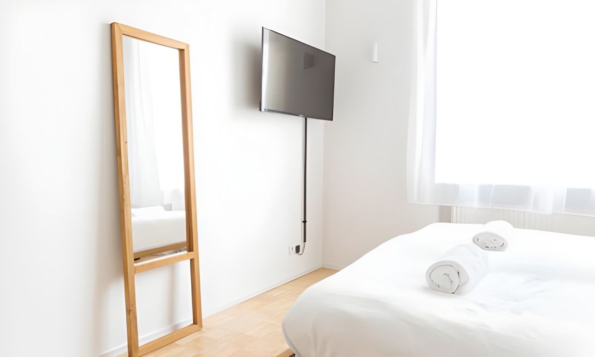 Chambre lumineuse avec un miroir et un lit blanc.